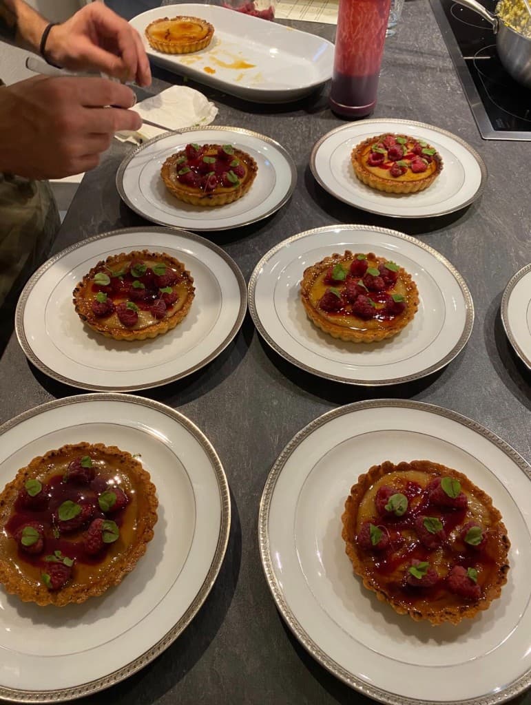 Tartelettes aux framboises en cours de finition, posées sur des assiettes à filet argenté